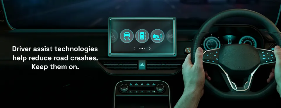 Image of hands on a driving wheel and driver assist technologies displayed on a large display.