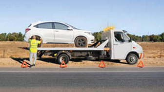 Tow truck with flashing lights loading a car on roadside, warning triangles placed for safety.